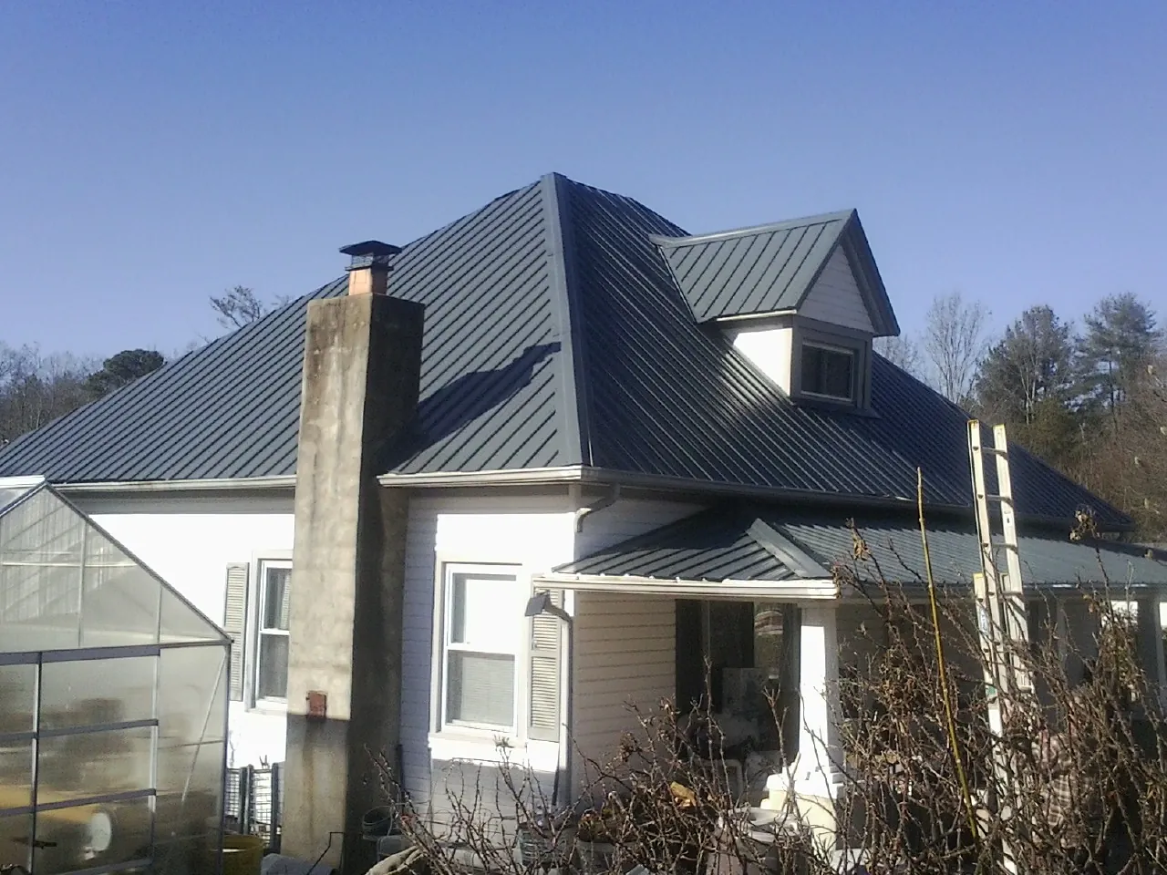 Dark blue standing seam metal roof on a white farmhouse with dormer — Slate & Tile Roof Repair by Roofing Brothers in Gerton