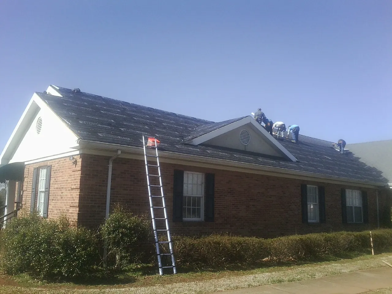 Crew tearing shingles off a brick ranch roof with a ladder set — Emergency Roof Repair work by our crew in Gerton