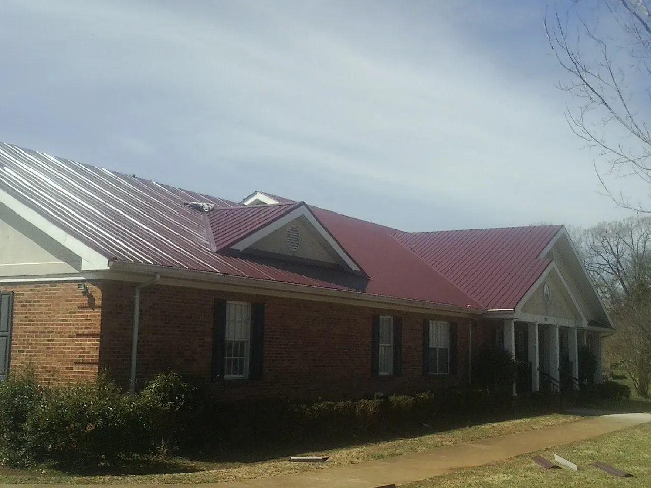 Red metal roof with gabled entries on a long brick building, from a Hail Damage Roof Repair job in Gerton
