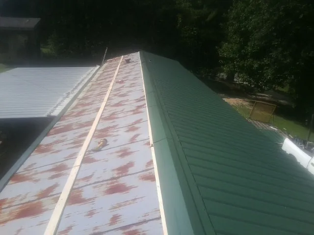 Old rusted panels beside newly installed green metal roofing — Wind Damage Roof Repair by Roofing Brothers in Gerton