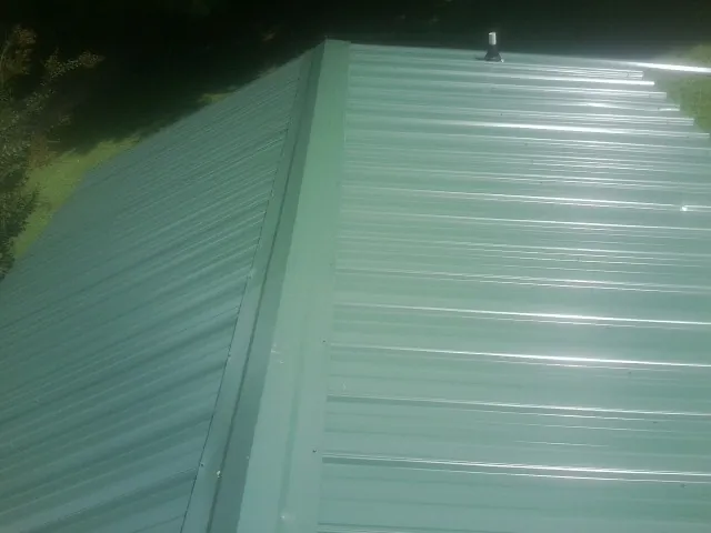 New green metal panels meeting at the ridge of a roof — Flat Roof Repair work by our crew in Gerton