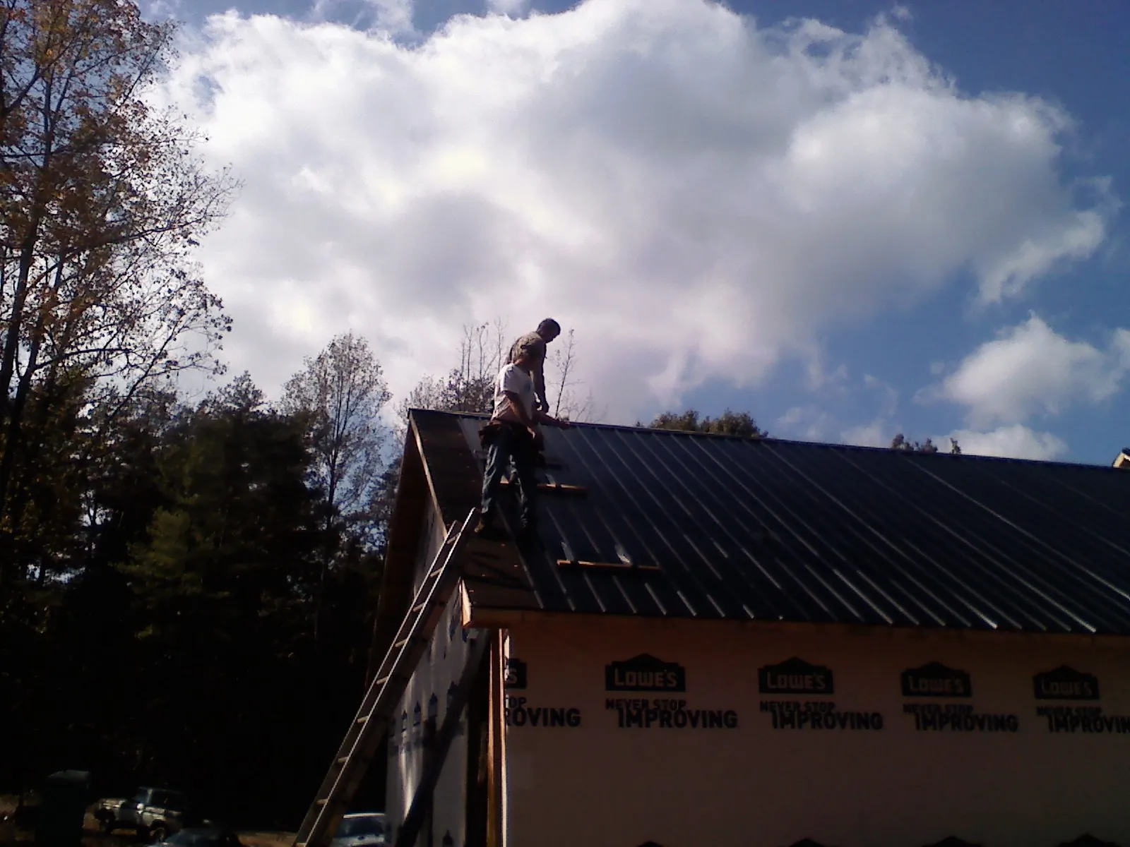 Roofer fastening dark metal panels high against a cloudy sky, from a Roof Inspection job in Gerton
