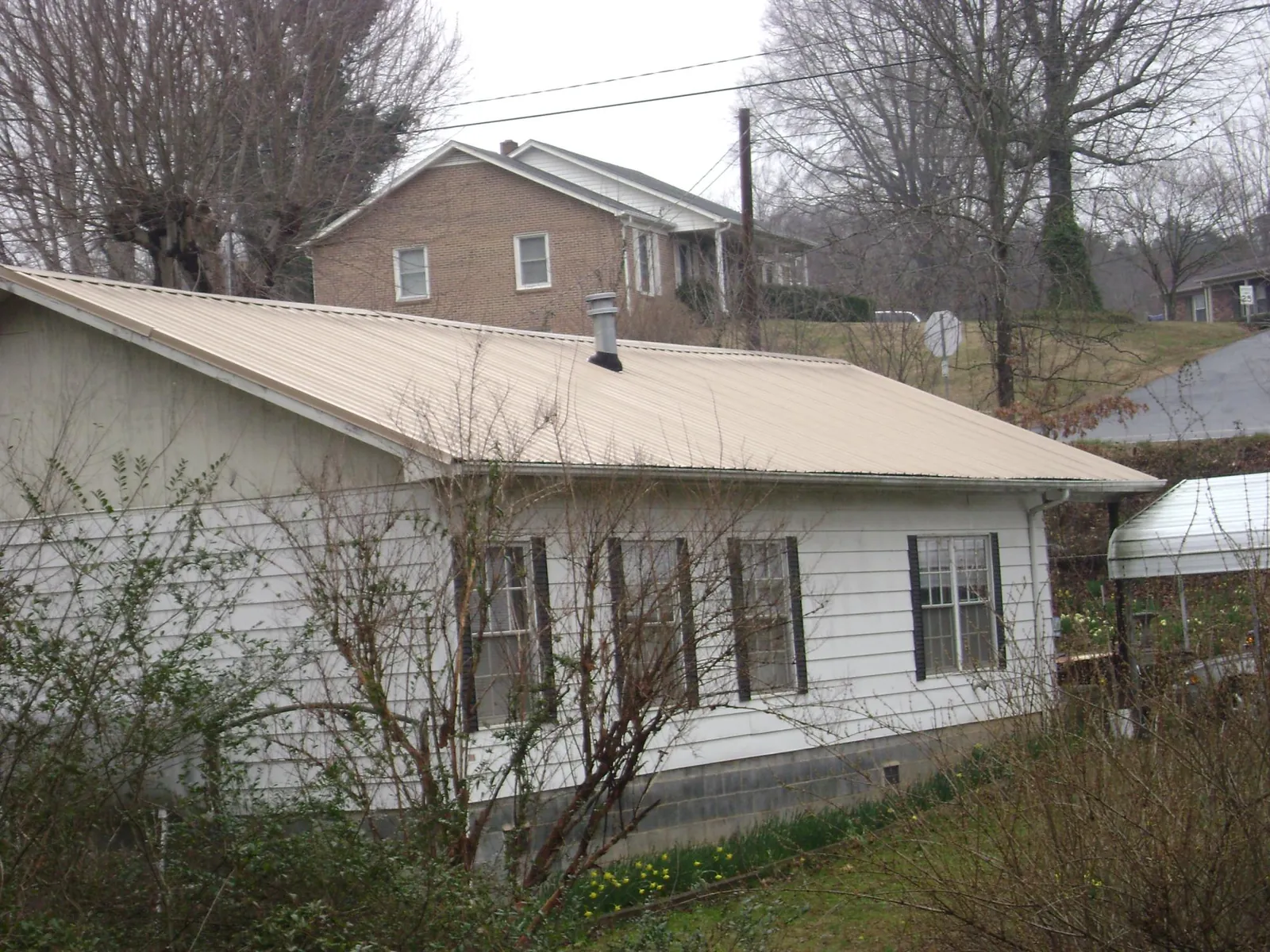 Tan metal roof on a white sided house set into a hillside — Commercial Roofing by Roofing Brothers in Gerton