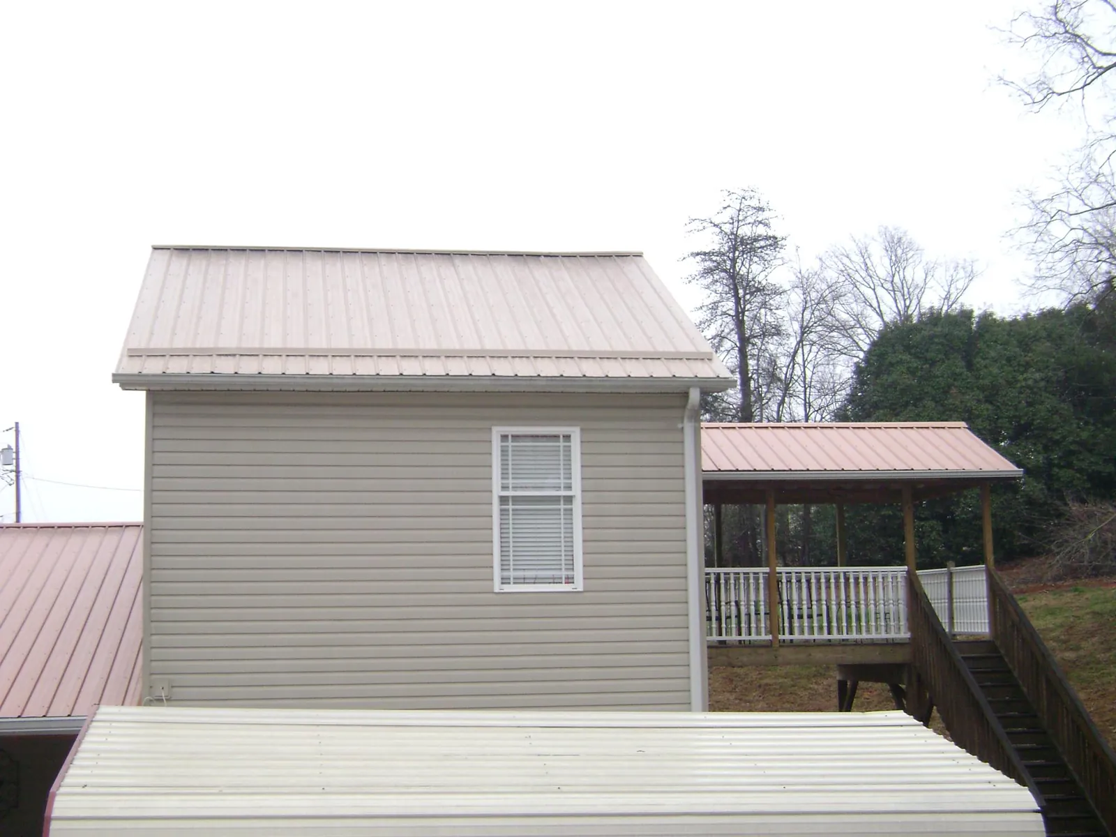 Tan metal roofs on a two story addition and attached porch, from a Roof Replacement job in Gerton